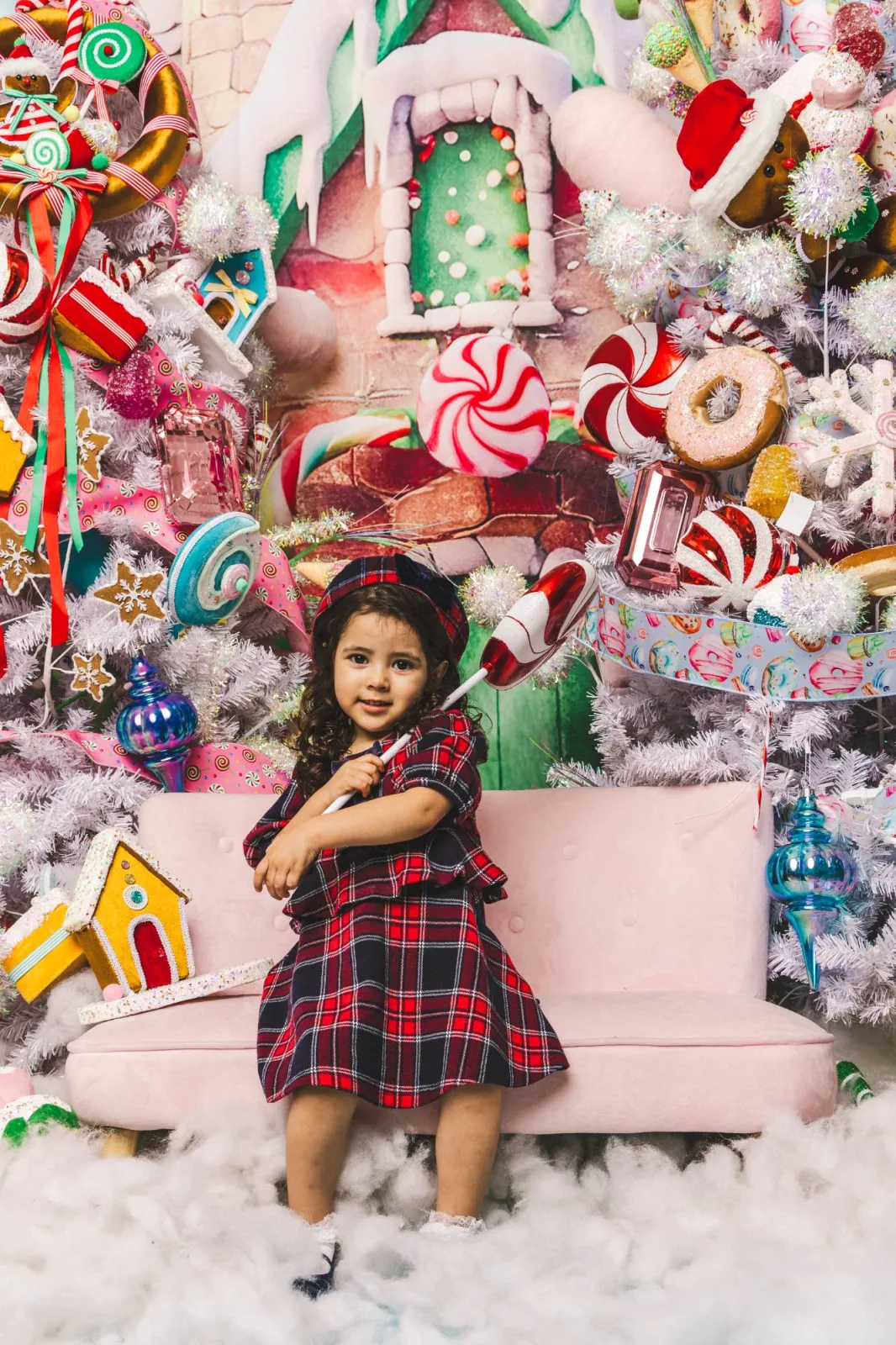 Toddler in tartan holding an oversized lollipop on a pink sofa in a candyland holiday set