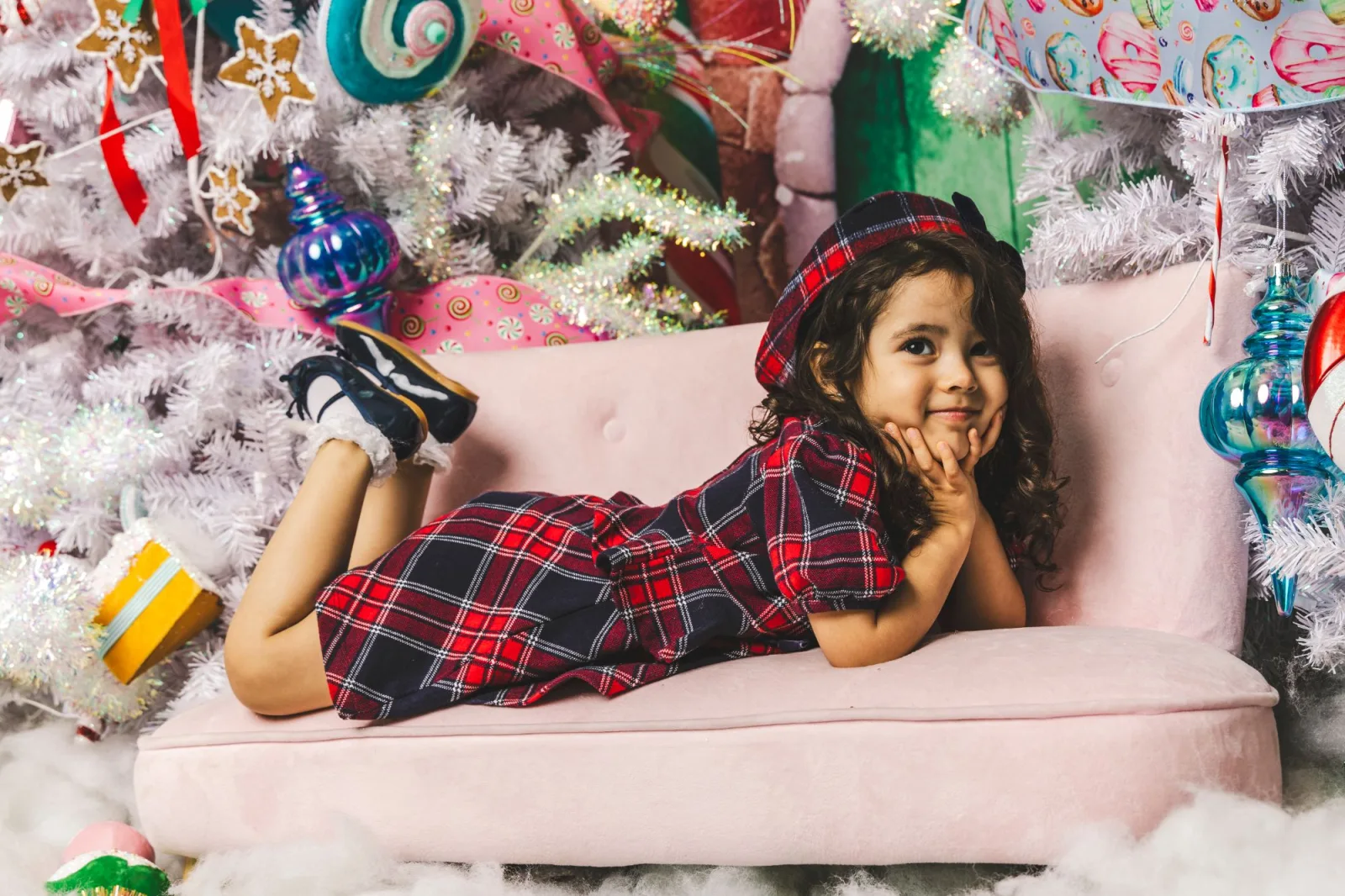 Toddler lounging on a pink sofa amid a candyland holiday set