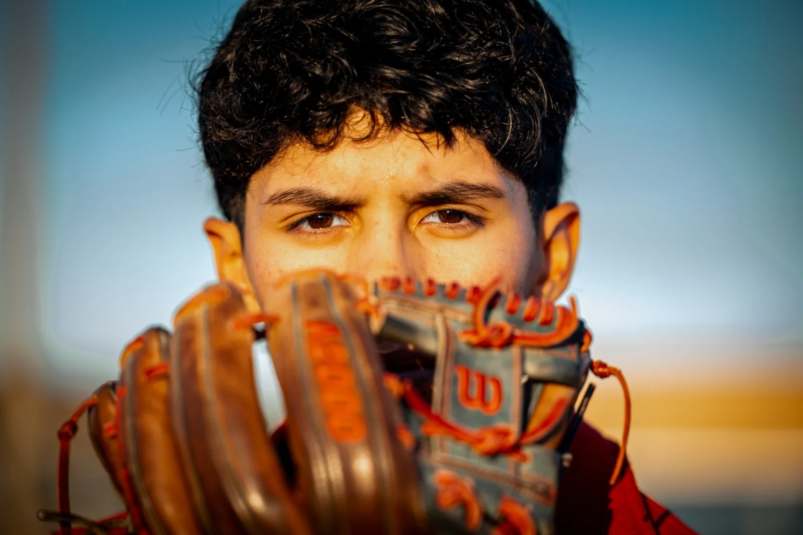 Close portrait of a senior holding his glove up beside his face in warm evening light